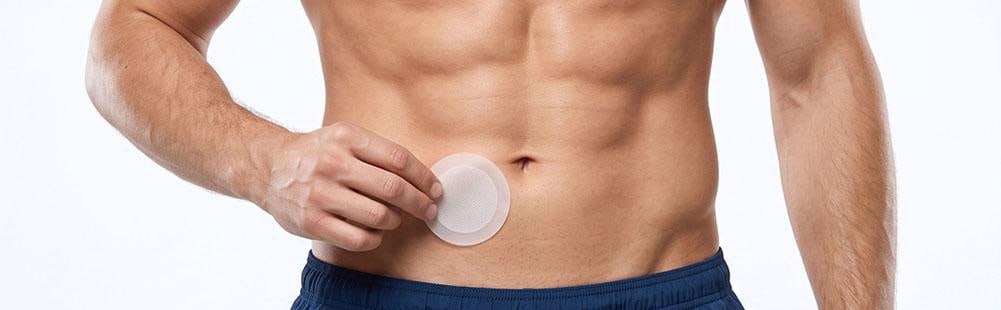 A hand pressing a Vigor Patch onto the lower belly, beside the navel