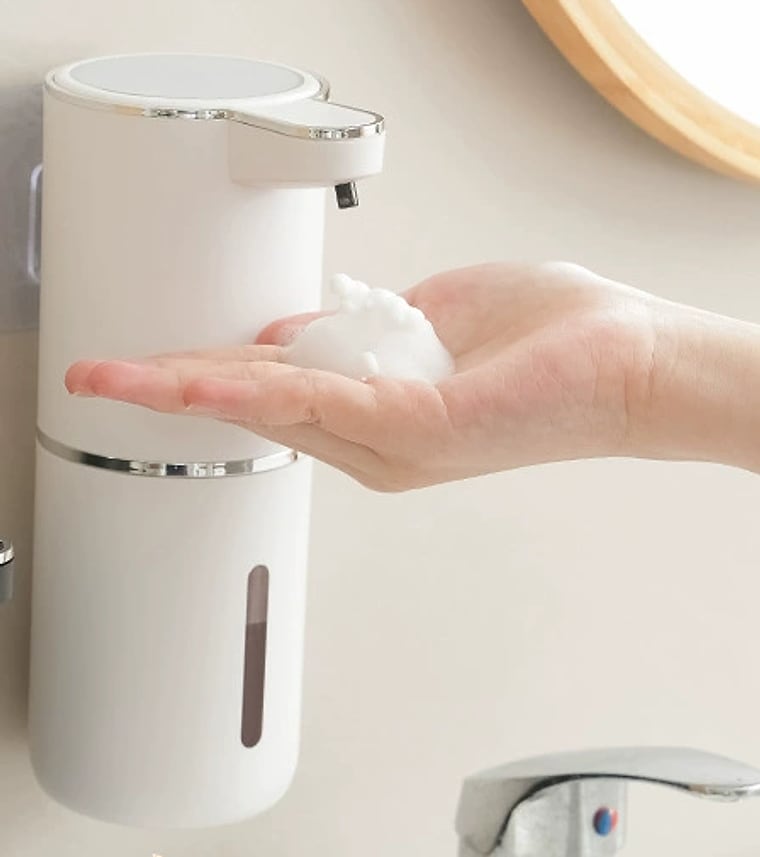 A hand getting foam from the Automatic Soap Dispenser on a wall